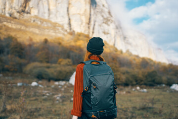 woman in a warm hat with a backpack on her back and in a sweater outdoors in the mountains gesticulate with her hands