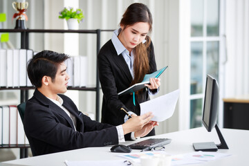 Two serious business colleagues discussing the project details and looking at the contract paper together while female co-worker writing notes in a notebook. Teamwork, collaboration concept.