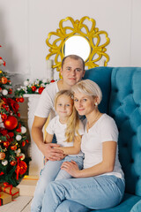 Beautiful young happy and cheerful family on an armchair near the New Year tree.