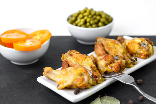 Chicken Wings With Spices, Cooked At Home In The Oven With Yellow Tomatoes And Green Peas, On A Dark Background. The Concept Of Home Cooking And Healthy Eating.