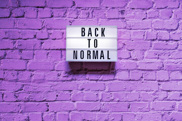 Fototapeta na wymiar Text Back to normal in lightbox on brick wall