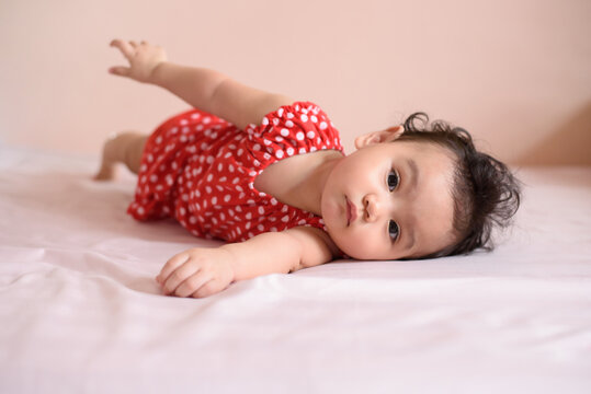 Little Asian wavy black hair baby, a cute toddler dressed in red lying on the bed and looking at camera