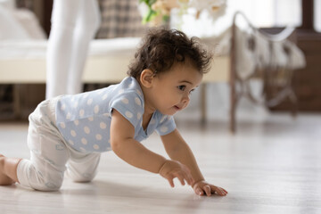 Cute little African American toddler baby child crawl on wooden floor at home play alone explore world. Small biracial girl kid learn walking try to make first steps. Childcare, upbringing concept.