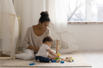 Loving happy young African American mother play with blocks brick with small toddler baby child....