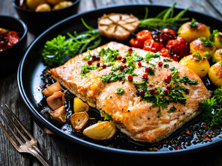 Roasted salmon steak with roast potatoes and vegetable salad served on black plate on wooden table
