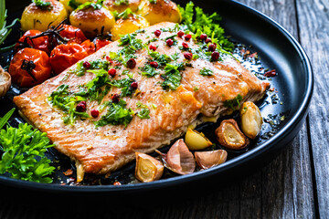Roasted salmon steak with roast potatoes and vegetable salad served on black plate on wooden table
