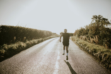 Obraz premium Man running in the countryside at sunset rear view
