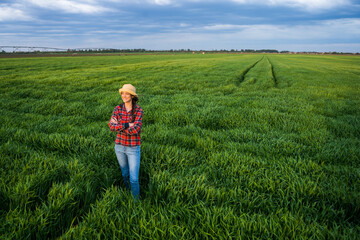 Naklejka na ściany i meble Proud female farmer is standing in her barley field and enjoying sunset.
