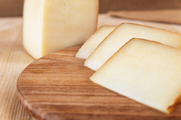 photo of slices of a typical Italian light-colored cheese, arranged on a dark wooden cutting board. around there are bay leaves, chilli and Apulian croutons. HD image for magazines, sites, social netw