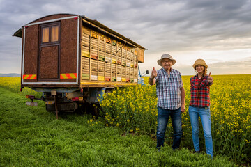 Proud two generations beekeepers are standing in front of their truck with beehives.