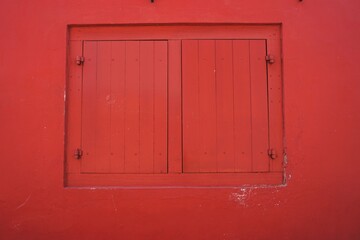 Pair of matching wooden panel window shutters framed in matching bright red horizontal wall