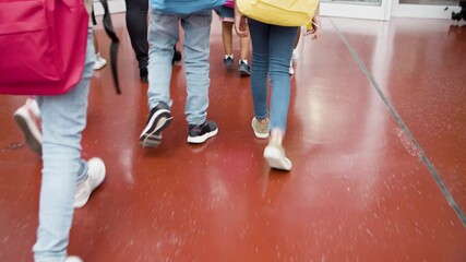 Close-up of children legs in school corridor. Tracking shot of schoolkids with colorful backpacks and teacher walking in hallway. Back to school concept. 