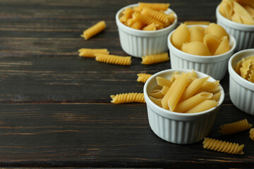 Bowls with uncooked pasta on wooden background