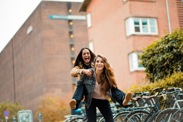 Two women having fun outside. Girl carrying friend on piggyback.  Piggyback ride.