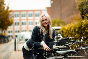 Fototapeta na wymiar Blond woman standing on street by the bicycle. Focus is on woman. Urban woman.