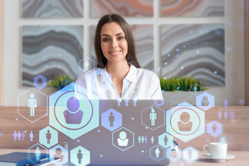 Attractive businesswoman in white shirt at workplace working with laptop to hire new employees for international business consulting. HR, social media hologram icons over office background