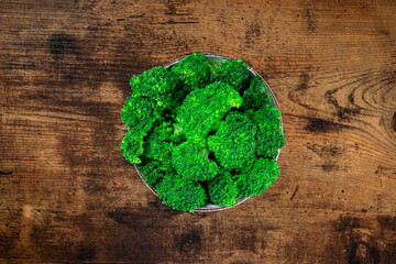 Cooked broccoli in a bowl, shot from the top on a dark rustic wooden backgroun