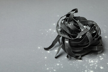 Black uncooked pasta with flour on gray background