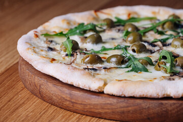 Appetizing Pizza on a wooden table in a restaurant. Close-up of melted cheese, olives, mushrooms, and herbs. Freshly cooked cheese pizza on a wooden board. Italian cuisine.