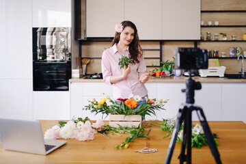 Young female florist record video tutorial of floral compositions design on camera, woman interior...