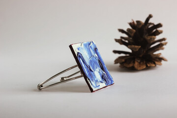 Handmade painted bracelet with blue texture near pine cone against a white background, isolated blue bracelet decorated with blue and white paint