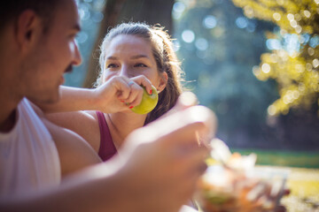 Fototapeta premium Couple in the park having break and eating healthy meal. Salad and apple. Focus is on woman.