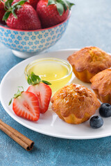 Healthy breakfast - vegan carrot muffins with honey, cinnamon, strawberry and blueberry on white plate. Blue stone background. Copy space.