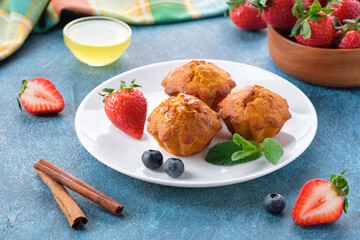Healthy vegan carrot muffins with cinnamon, honey, mint leaves, strawberry and blueberry on white plate. Blue stone background. Close up.