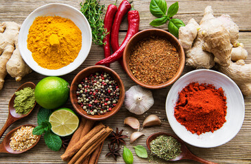 A selection of various colorful spices on a wooden table in bowls and spoons
