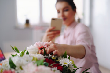 Flower shop: a girl florist photographs a flower composition on a smartphone for social networks.