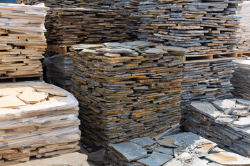 Natural stone blocks packed in stacks are stored on ground outdoors at a hardware store warehouse