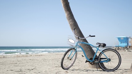 Blue bicycle, cruiser bike by ocean beach, pacific coast, Oceanside California USA. Summertime vacations, sea shore. Vintage cycle on sand near lifeguard tower or watchtower hut. Sky and water waves.