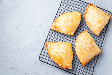 Homemade small peach and cinnamon hand pies with crust dough,  sprinkled with sugar, on cooling rack, top view, horizontal, copy space