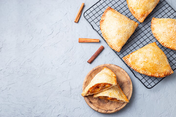 Small peach and cinnamon hand pies with crust dough,  sprinkled with sugar, on wooden plate and cooling rack, top view, horizontal, copy space