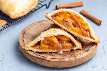 Homemade small peach and cinnamon hand pies with crust dough,  sprinkled with sugar, on wooden plate closeup, horizontal © iuliia_n