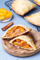 Homemade small peach and cinnamon hand pies with crust dough,  sprinkled with sugar, on wooden plate and cooling rack, vertical