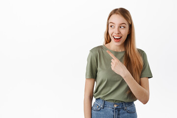 Obraz premium Happy smiling female model pointing, looking left and laughing over banner, showing something funny aside, standing in t-shirt against white background