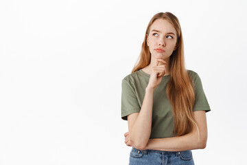 Thoughtful young woman making serious decision, looking up while pondering choices, frowning while...