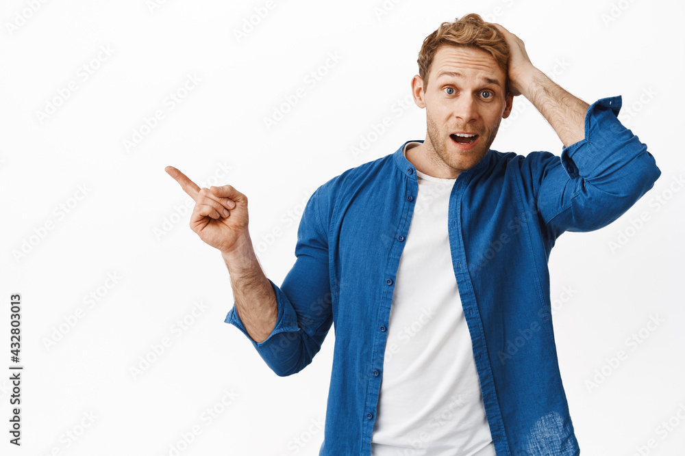 Wall mural Confused guy scratch head and pointing left at something surprising, looking questioned, asking question about product banner, standing over white background clueless - Wall murals