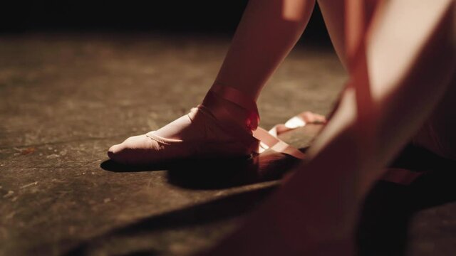 Ballerina Seated On The Floor Tying Her Ballet Shoes Inside The Studio. - Selective Focus Shot