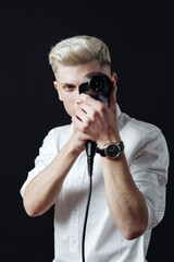 Portrait of stylish professional hairdresser with blond hair. Man wearing white shirt, looking aside and holding a blow dryer near his face