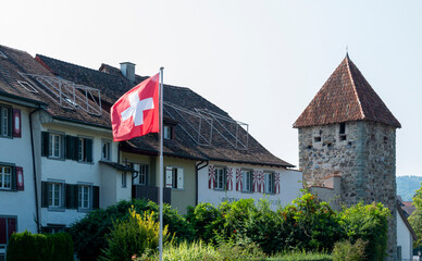 Fototapeta na wymiar Stein am Rhein, Switzerland - Swiss flag blowing on the wind on a Hexenturm historic tower background in a old touristic town in Switzerland