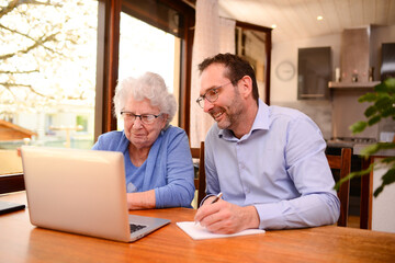 mature man helping elderly senior woman at home with paperwork and computer internet lesson - Powered by Adobe