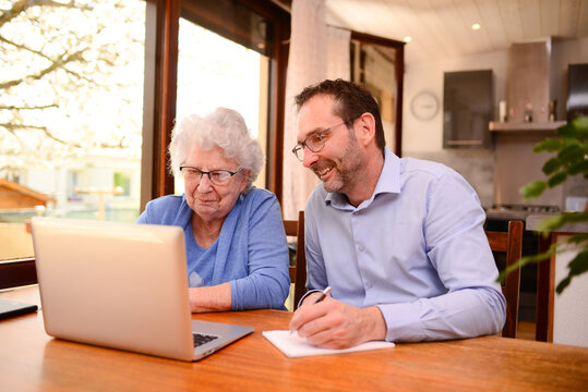 mature man helping elderly senior woman at home with paperwork and computer internet lesson