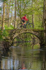 Naklejka premium nice active senior woman riding her electric mountain bike in early spring along the little river Glems near Stuttgart, Baden-Wuerttemberg, Germany 