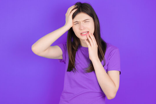 Young gloomy young beautiful Caucasian woman wearing purple T-shirt over purple wall, hiding face with hands pouting and crying, standing upset and depressed complaining about job problem.