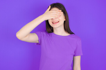 Happy young beautiful Caucasian woman wearing purple T-shirt over purple  closing eyes with hand going to see surprise prepared by friend standing and smiling in anticipation for something wonderful.