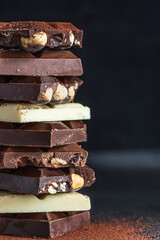 Stack of milk and dark chocolate with nuts, caramel and fruits and berries on dark marble background..
