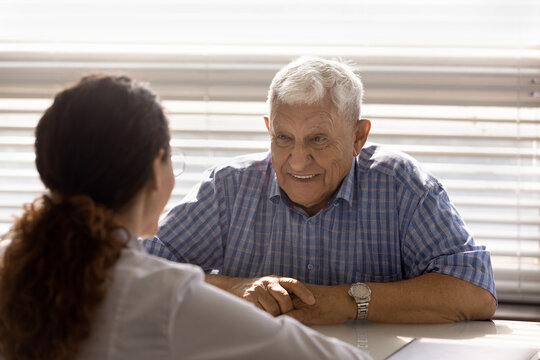 Conversing with doc. Smiling mature male patient sit at doctor office feel satisfied getting good service at trusted clinic. Happy old man listen to gp speaking about positive changes in test results