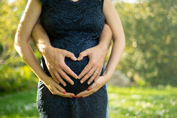 Ein Mann umarmt von hinten seine schwangere Frau und formt mit seinen Händen ein Herz auf Ihrem...